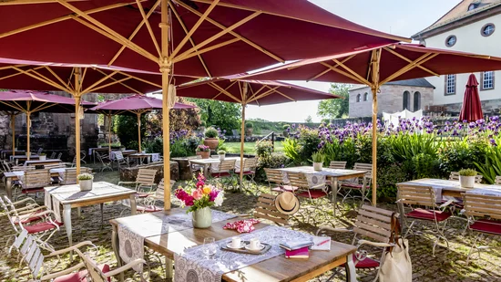 Sonnige Terrasse mit roten Sonnenschirmen, Tischen und Stühlen im Garten