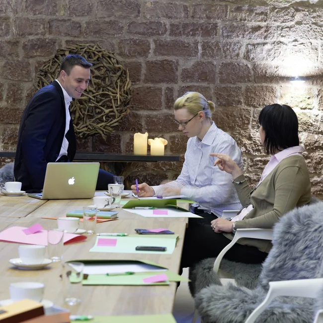 Drei Personen bei Besprechung an einem Tisch mit Laptop und Notizen