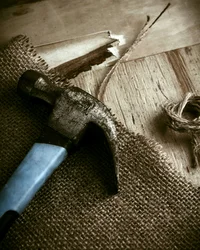 Alter Hammer liegt auf sackartigem Stoff neben Holzbrett und Seil