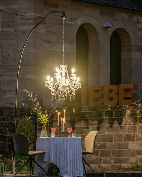 Beleuchteter Kronleuchter über gedecktem Tisch mit Kerzen und zwei Stühlen außen