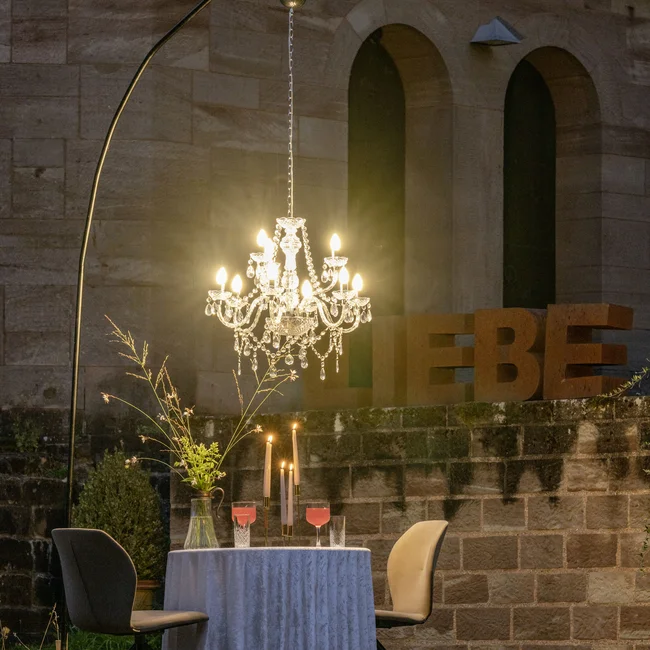 Beleuchteter Kronleuchter über gedecktem Tisch mit Kerzen und zwei Stühlen außen