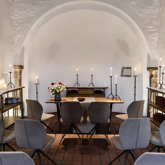 Kleiner, ruhiger Raum mit Stühlen, Kerzen und einem Tisch mit Blumen