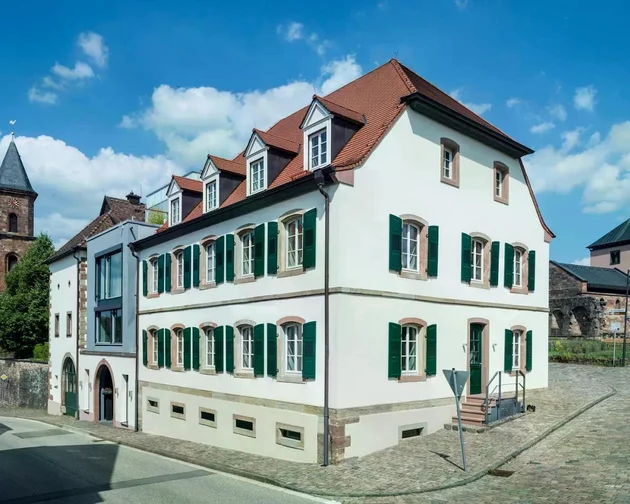 Historisches Gebäude mit grünem Fensterläden und rotem Dach an einer Kopfsteinpflasterstraße