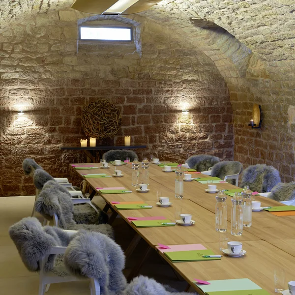 Konferenzraum mit langem Holztisch und Stühlen mit Fellbezügen in einem Gewölbe