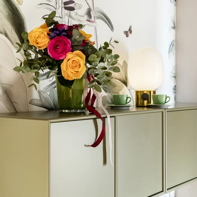 Blumenstrauß auf grünem Wandregal vor floralem Hintergrund