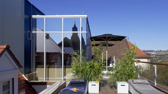 Dachterrasse mit Liegestühlen, Pflanzen und Spiegelung eines Kirchturms im Fenster