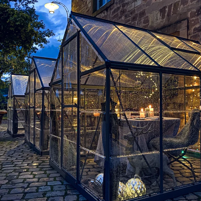 Mehrere beleuchtete Glashäuser mit Kerzen auf Kopfsteinpflaster bei Abenddämmerung