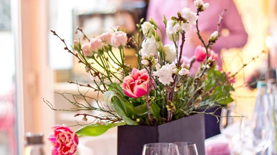 Blumenstrauß mit rosa und weißen Blüten in schwarzem Vase auf gedecktem Tisch