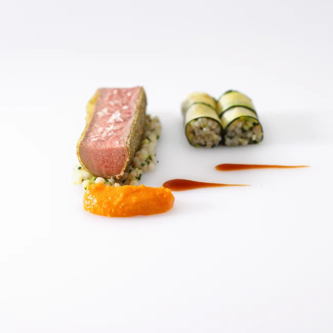 Fein angerichtetes Gericht mit Fleisch, Gemüse und Saucen auf weißem Teller