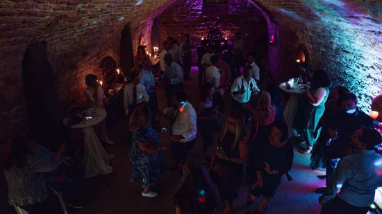 Menschen tanzen und unterhalten sich in einem dunklen, beleuchteten Steinkeller