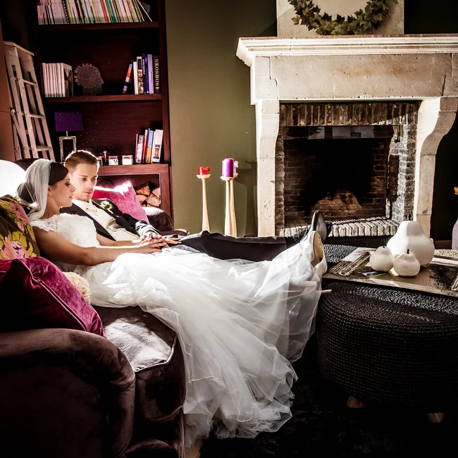 Brautpaar sitzt entspannt auf einem Sofa vor einem Kamin in einem gemütlichen Wohnzimmer