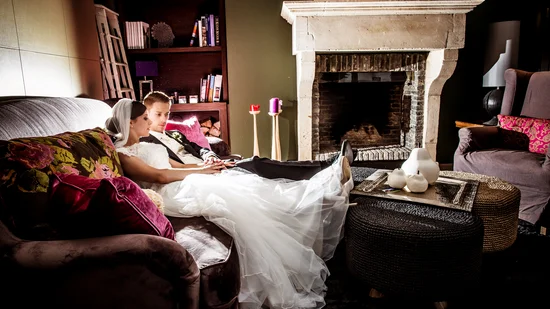 Brautpaar sitzt entspannt auf einem Sofa vor einem Kamin in einem gemütlichen Wohnzimmer