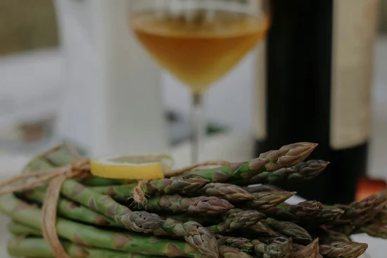 Bündel grüner Spargel mit Zitronenscheibe auf weißem Teller und Glas Weißwein