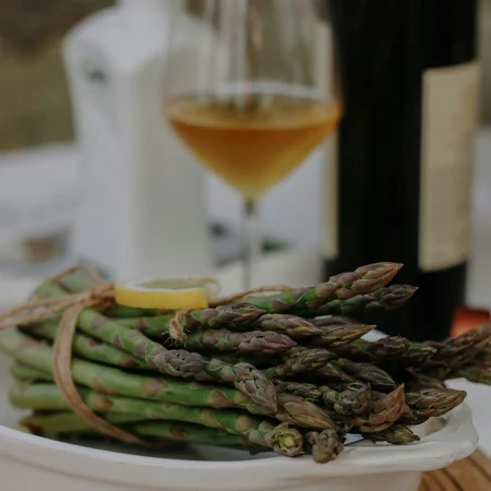 Bundle of green asparagus with lemon slice on white plate and glass of white wine