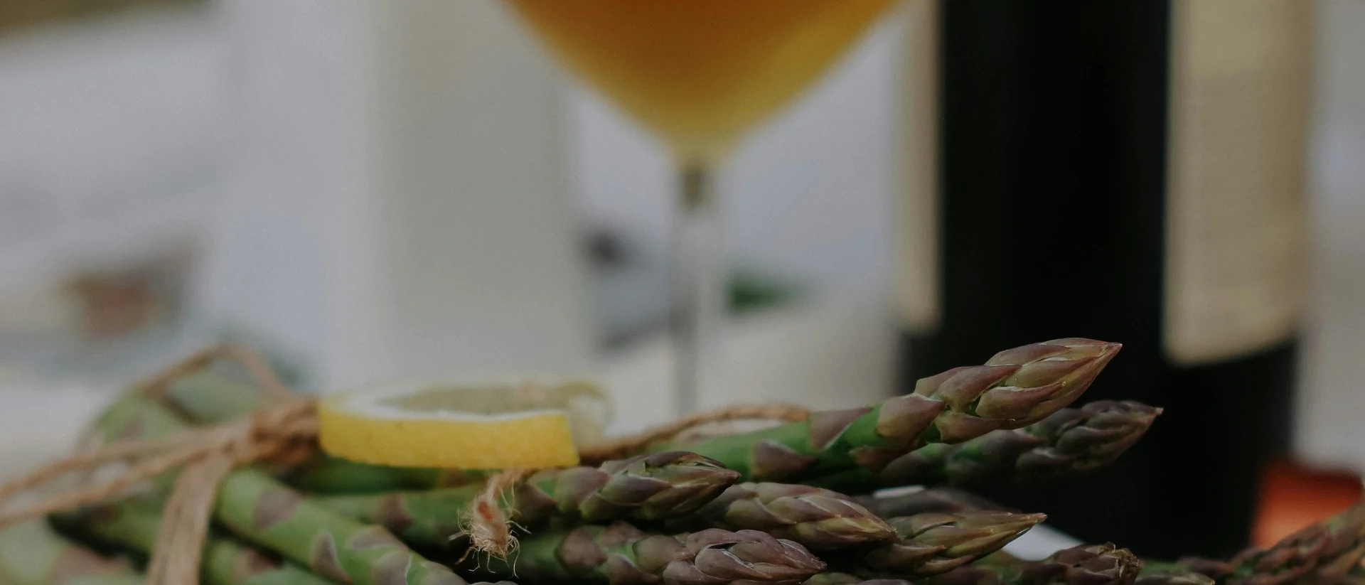 Prost auf den Spargel Bündel grüner Spargel mit Zitronenscheibe auf weißem Teller und Glas Weißwein