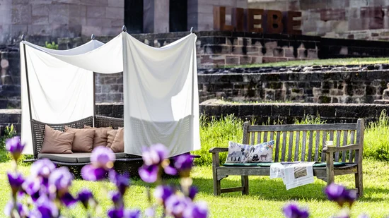 Gartenbereich mit Holzbank, gepolstertem Sitz und dem Schriftzug LIEBE im Hintergrund
