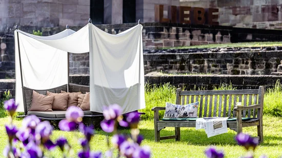 Gartenbereich mit Holzbank, gepolstertem Sitz und dem Schriftzug LIEBE im Hintergrund