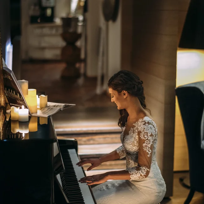 Braut im weißen Kleid spielt bei Kerzenlicht Klavier in gemütlichem Raum