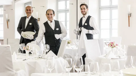 Drei Kellner bereiten ein elegantes Restaurant mit weißen Tischdecken vor