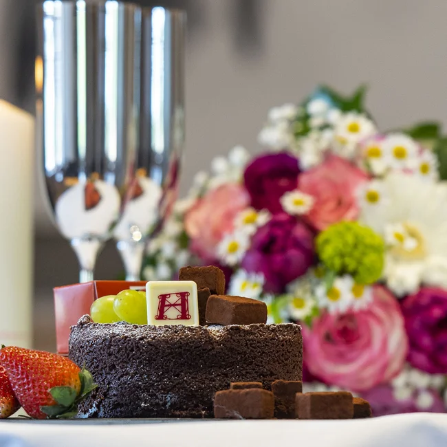 Schokoladenkuchen mit Früchten, Kerze, Sektgläser und Blumenstrauß auf Tisch