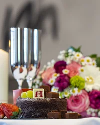 Schokoladenkuchen mit Früchten, Kerze, Sektgläser und Blumenstrauß auf Tisch