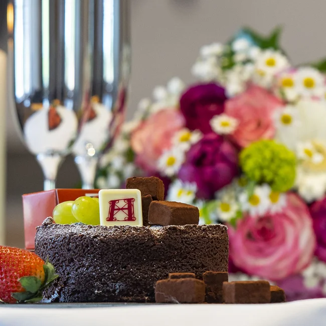 Schokoladenkuchen mit Früchten, Kerze, Sektgläser und Blumenstrauß auf Tisch