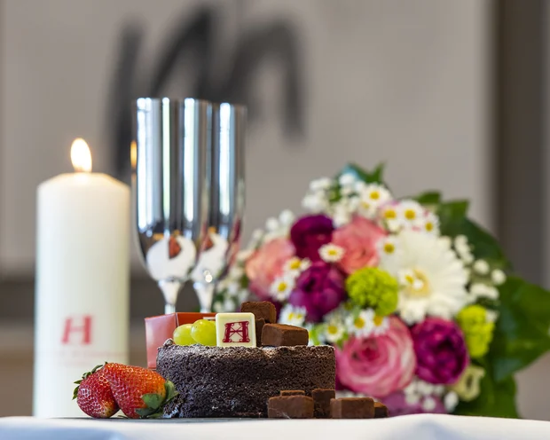 Schokoladenkuchen mit Früchten, Kerze, Sektgläser und Blumenstrauß auf Tisch