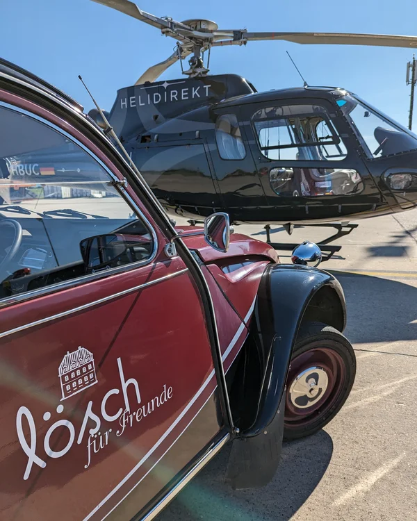Rotes Auto mit Lösch Werbung neben schwarzem Helikopter Helidirekt auf Flughafen