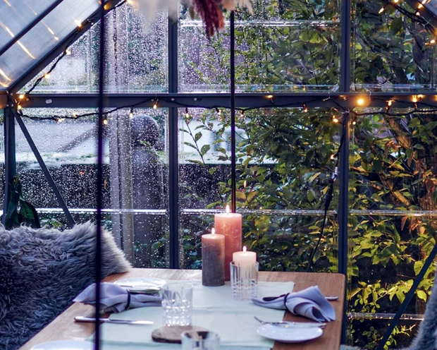 Gemütlich gedeckter Tisch in einem Glashaus mit Kerzen und Sitzkissen