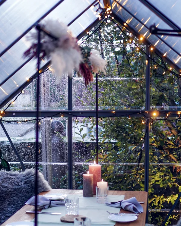 Gemütlich gedeckter Tisch in einem Glashaus mit Kerzen und Sitzkissen