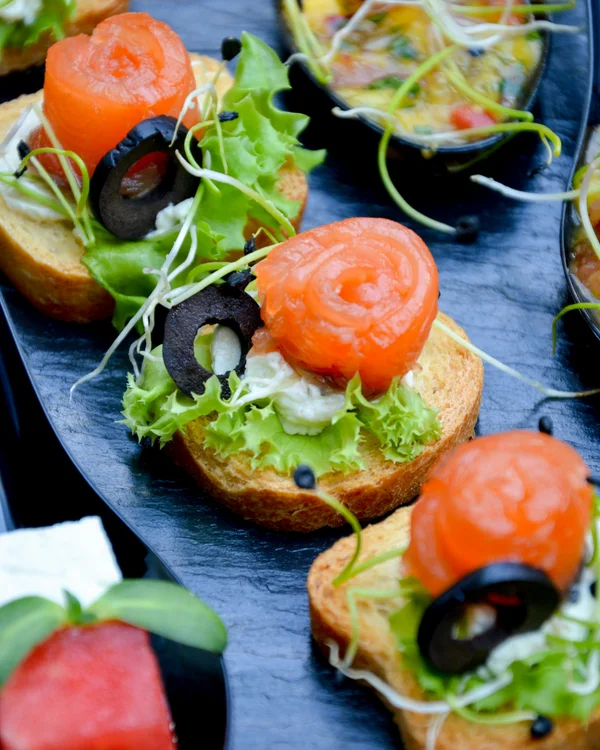 Platte mit Canapés aus Lachs, Salat und Oliven auf Baguette