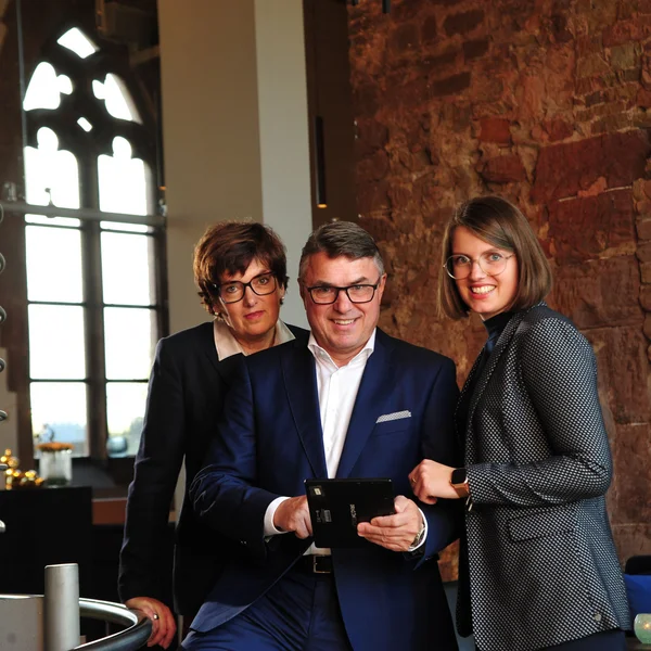 Drei Geschäftsleute lächeln, während sie gemeinsam ein Tablet benutzen