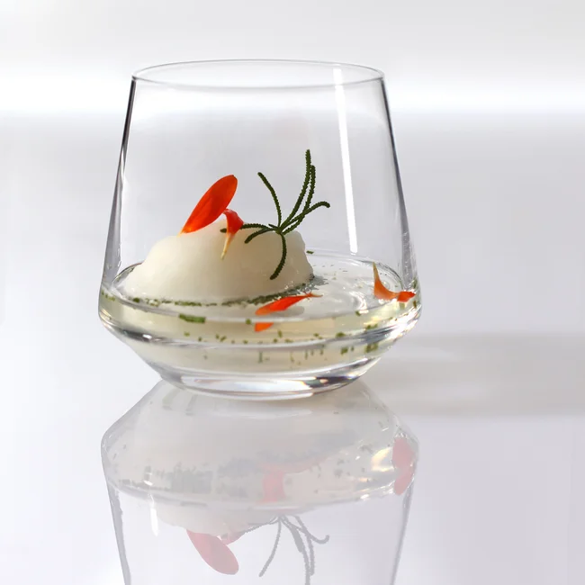 Moderner Cocktail mit rosa Blütenblättern und Kräutern in Glas mit Spiegelung