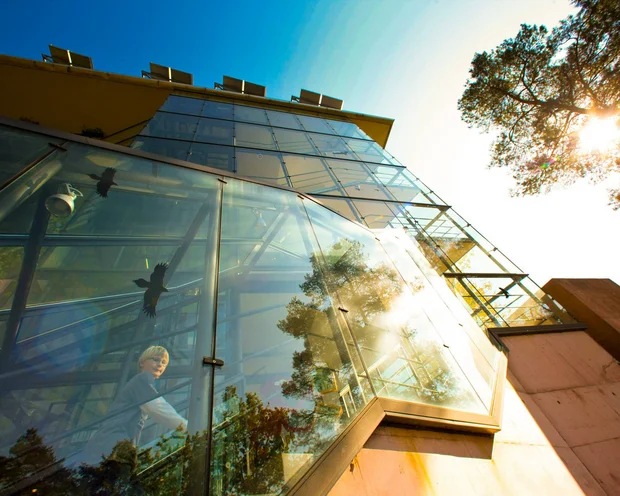 Moderne Glasfassade mit Reflexionen, Person treppt ein, sonniger Himmel