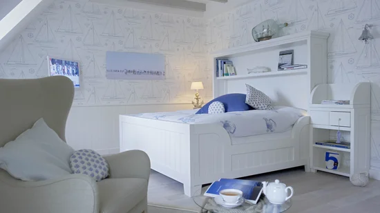Helles Schlafzimmer mit weißem Bett, blau-weißem Dekor und maritimem Muster