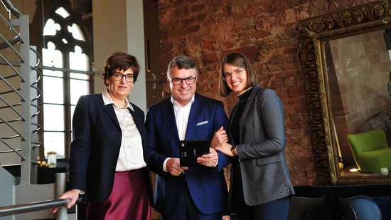 Drei Geschäftsleute stehen vor Backsteinwand in modernem Büro