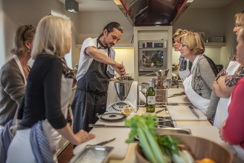 Koch demonstriert Kochtechnik vor einer Gruppe von Erwachsenen in einer Küche