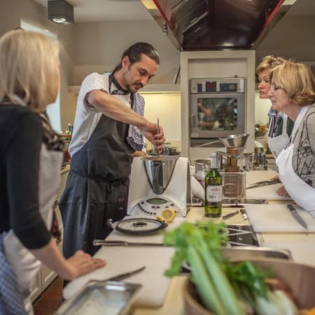 Koch demonstriert Kochtechnik vor einer Gruppe von Erwachsenen in einer Küche