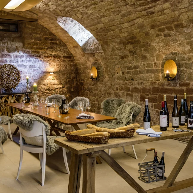 Weinkeller mit rustikalem Holz, Fellen auf Stühlen und Weinflaschen auf einem Tisch