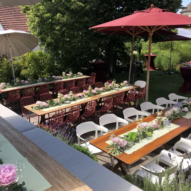 Gedeckte Tische mit Blumen und Sonnenschirmen in einem Garten bei Sonnenschein