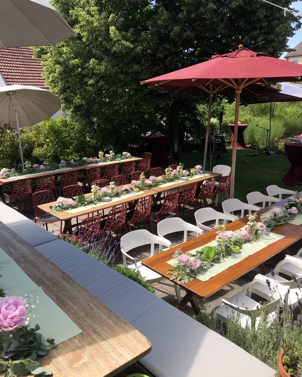 Gedeckte Tische mit Blumen und Sonnenschirmen in einem Garten bei Sonnenschein