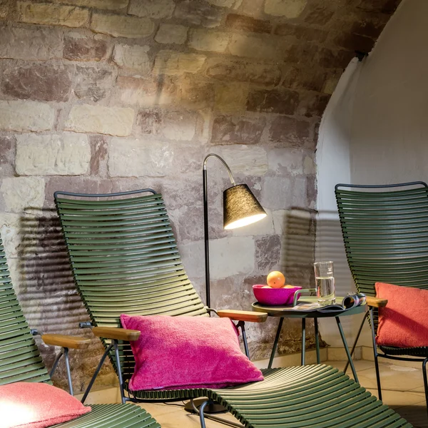Grüne Liegestühle mit pinken Kissen und Lampe vor einer Steinwand