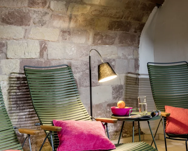 Grüne Liegestühle mit pinken Kissen und Lampe vor einer Steinwand
