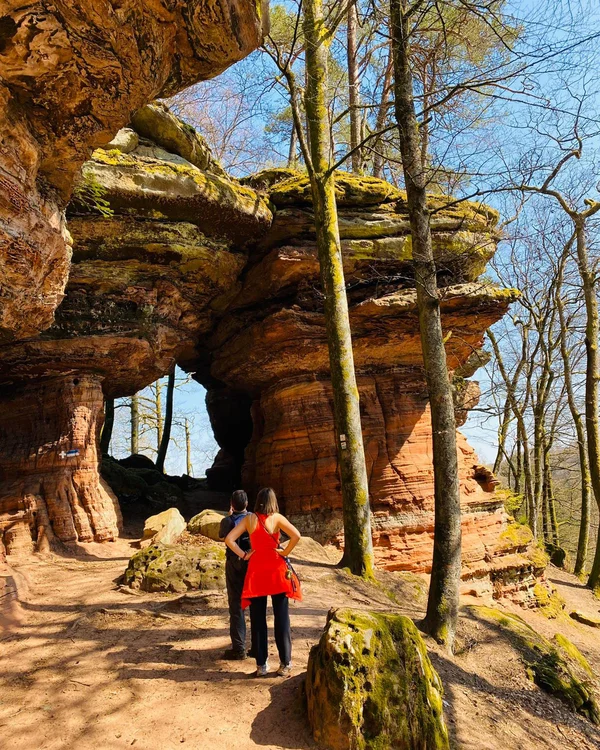 Wanderer vor einem großen Felsen mit natürlichem Durchgang im Wald