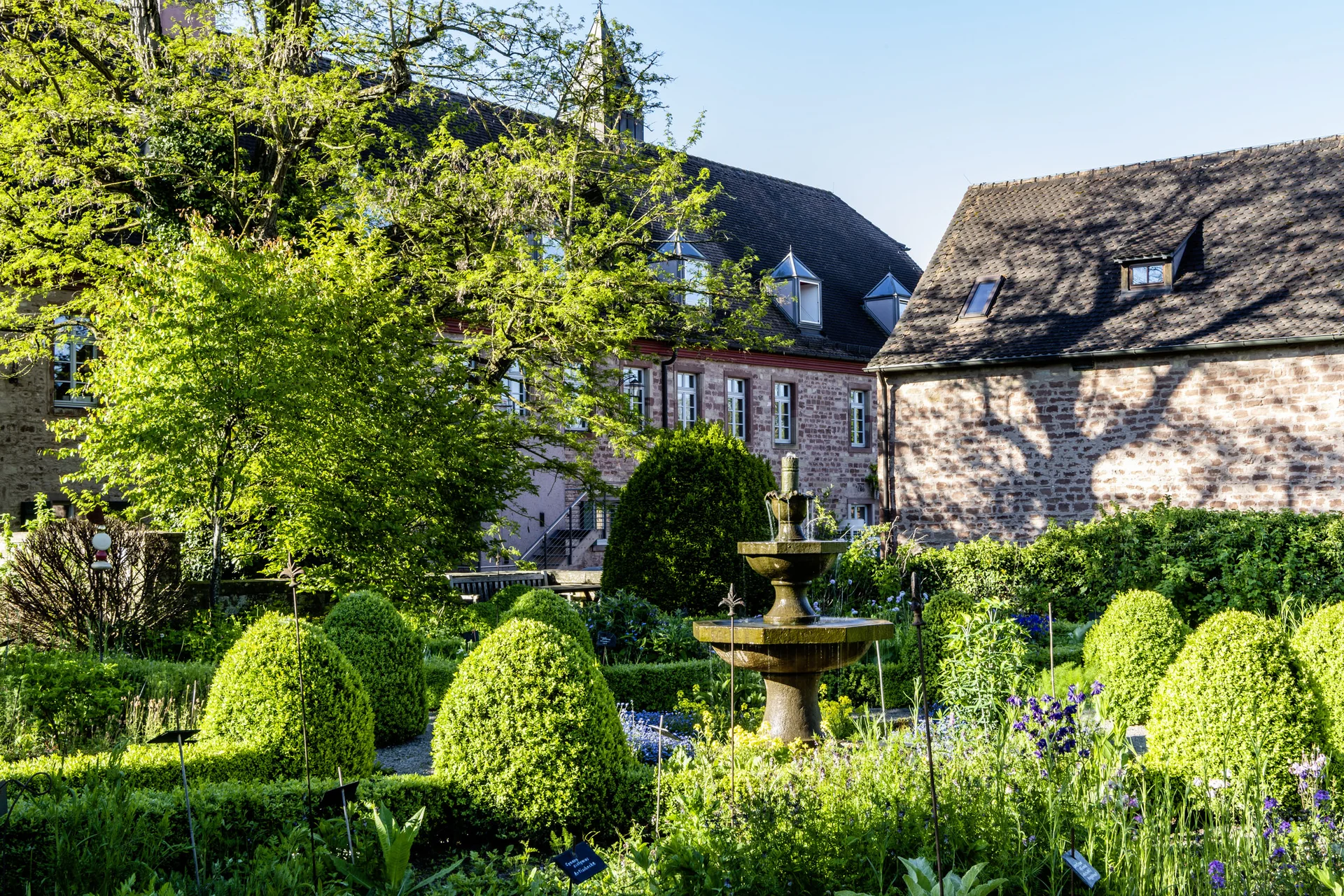 Historischer Garten mit Springbrunnen und Fachwerkhäusern im Hintergrund bei Sonnenschein