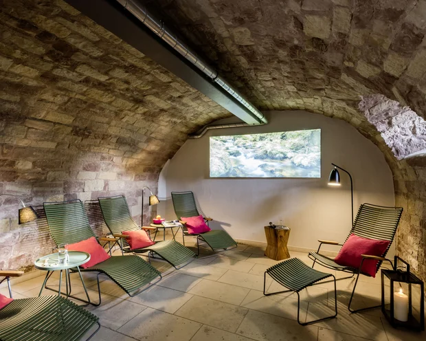 Entspannungsraum mit grünen Liegestühlen und roten Kissen in einem Gewölberaum