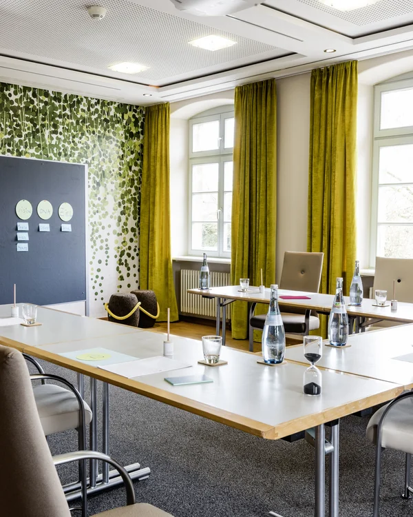 Konferenzraum mit grünen Vorhängen, Tischen, Stühlen und Flipchartwand