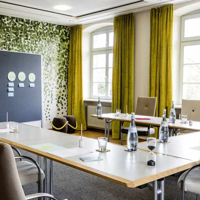 Konferenzraum mit grünen Vorhängen, Tischen, Stühlen und Flipchartwand