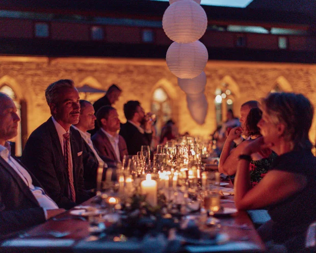 Abendessen im Freien mit Kerzen und Laternen, Menschen in formeller Kleidung sitzen am Tisch