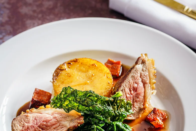 Elegantes Gericht mit rosa gebratenem Fleisch, Blattgemüse, Kartoffel und Würfeln